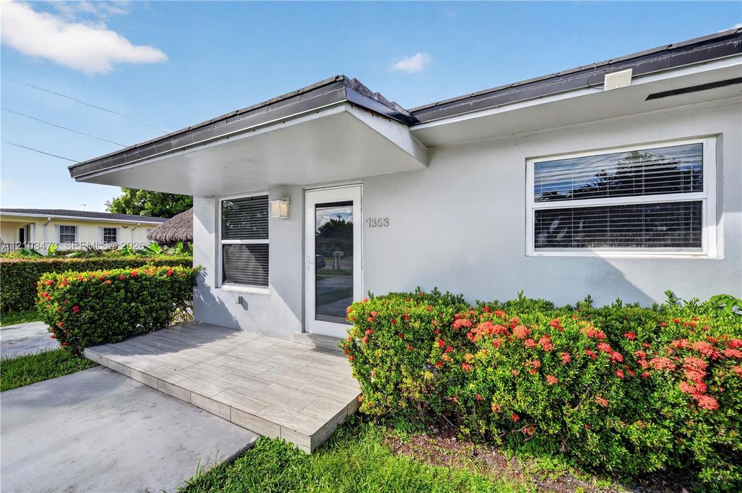 Stucco exterior with a covered entry, dark-framed windows, and decorative landscaping