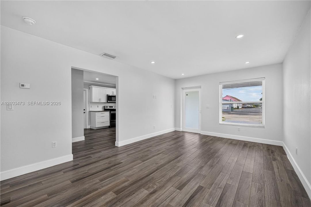 Expansive living space featuring wood-finish flooring, recessed lighting, and a kitchen with white cabinetry and black appliances