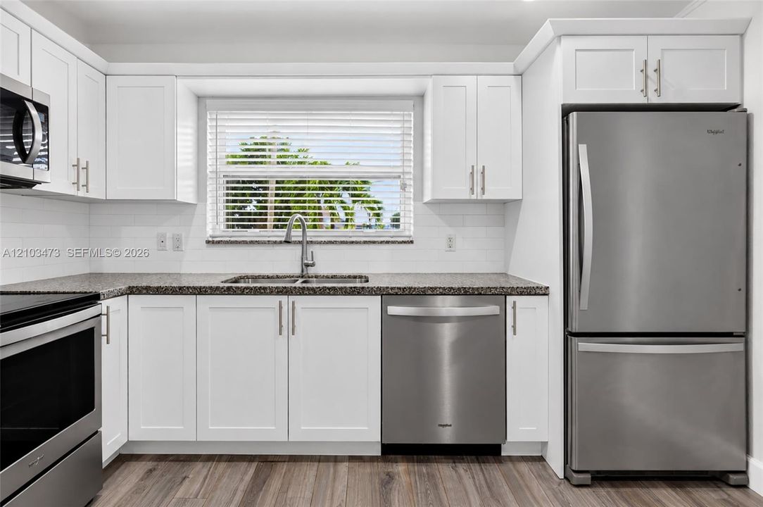 Modern kitchen featuring white shaker cabinetry, stainless steel appliances, granite countertops, and wood-finish flooring