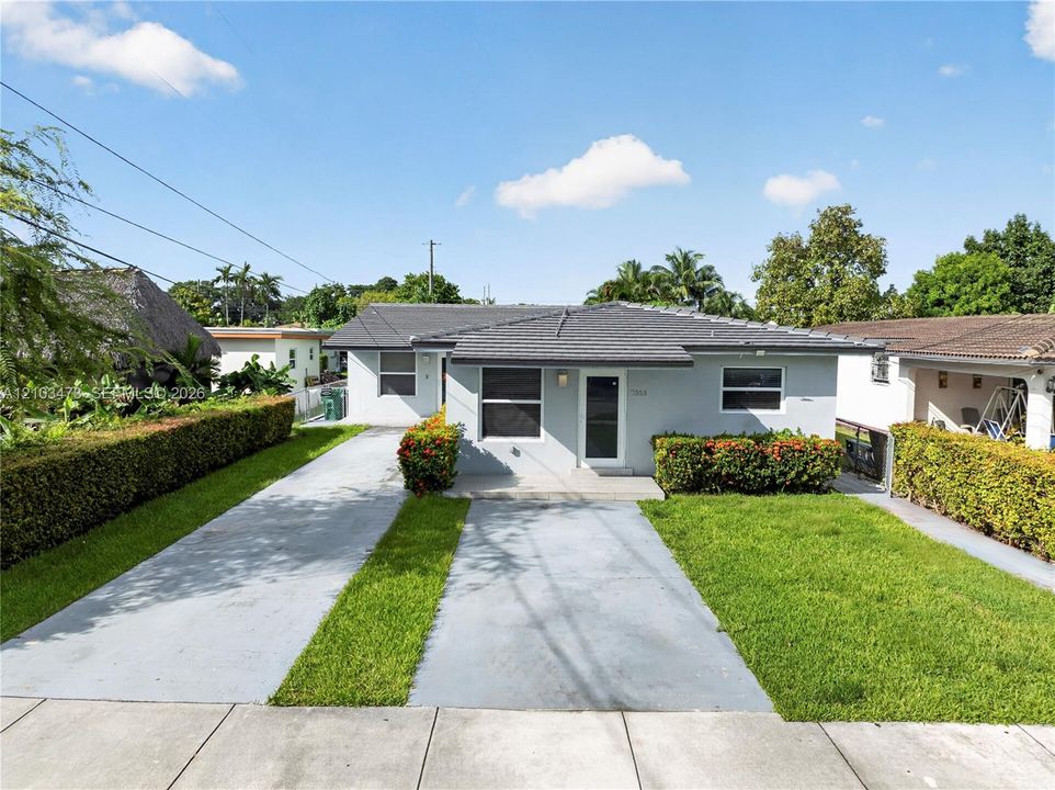 Single-story residence featuring a gray exterior, dark tile roof, and a concrete driveway with a central grass strip