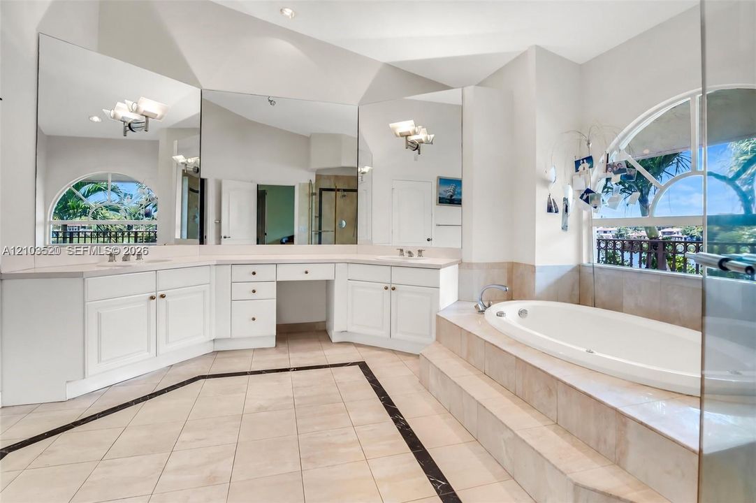 Bathroom featuring a dual-sink vanity with built-in cabinetry, an arched window, a raised soaking tub, and floor-to-ceiling mirrors