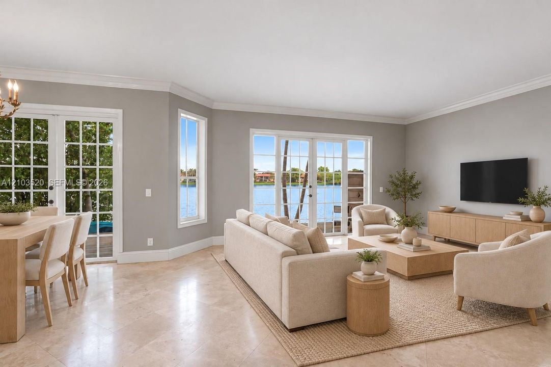 Neutral-toned living space featuring light stone flooring, crown molding, multiple sets of glass-paneled double doors, and expansive water scenery