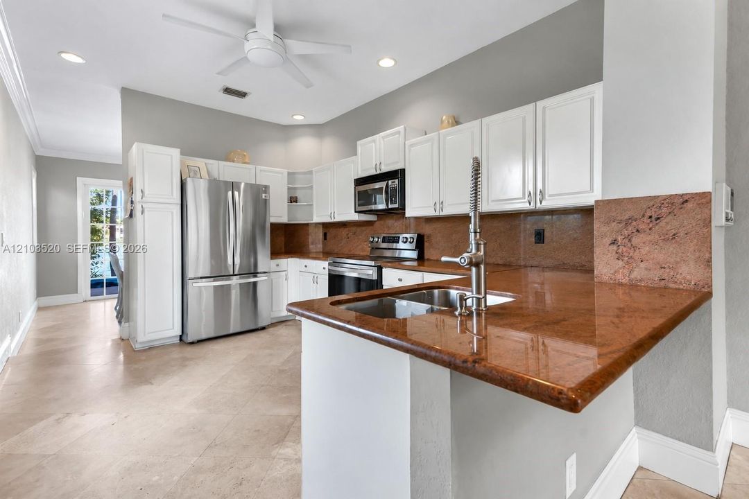 Kitchen featuring white cabinetry, polished stone countertops with matching backsplash, stainless steel appliances, and tile flooring