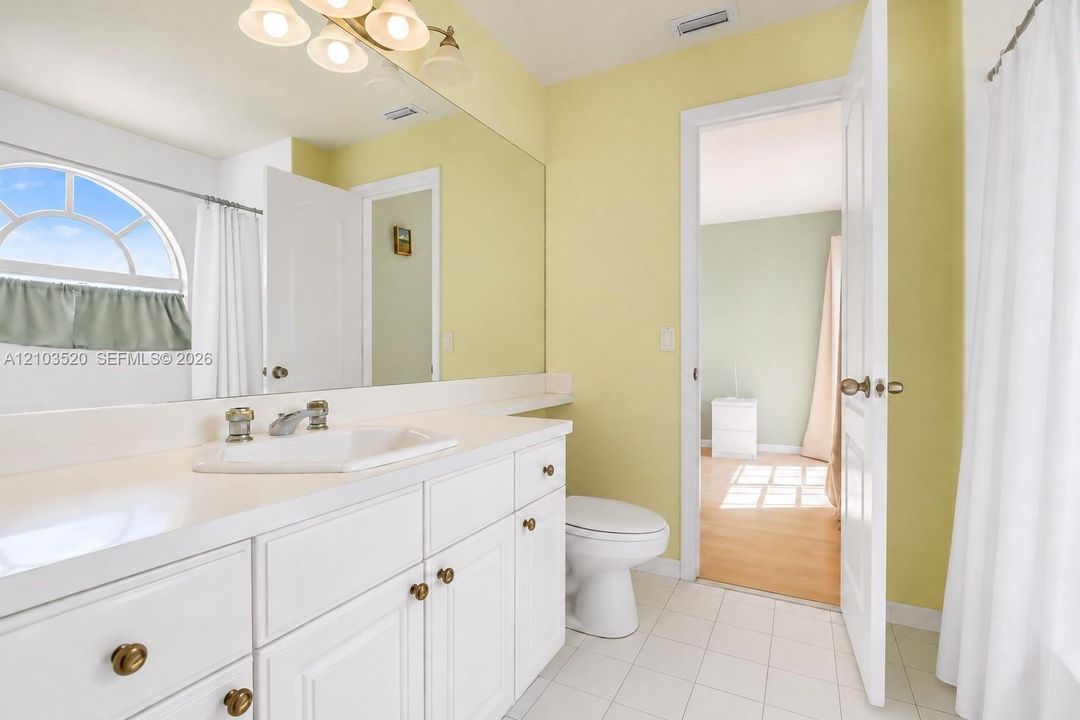 Bathroom featuring a white vanity with integrated sink, expansive wall-mounted mirror, polished chrome faucet, arched window, and ceramic tile flooring
