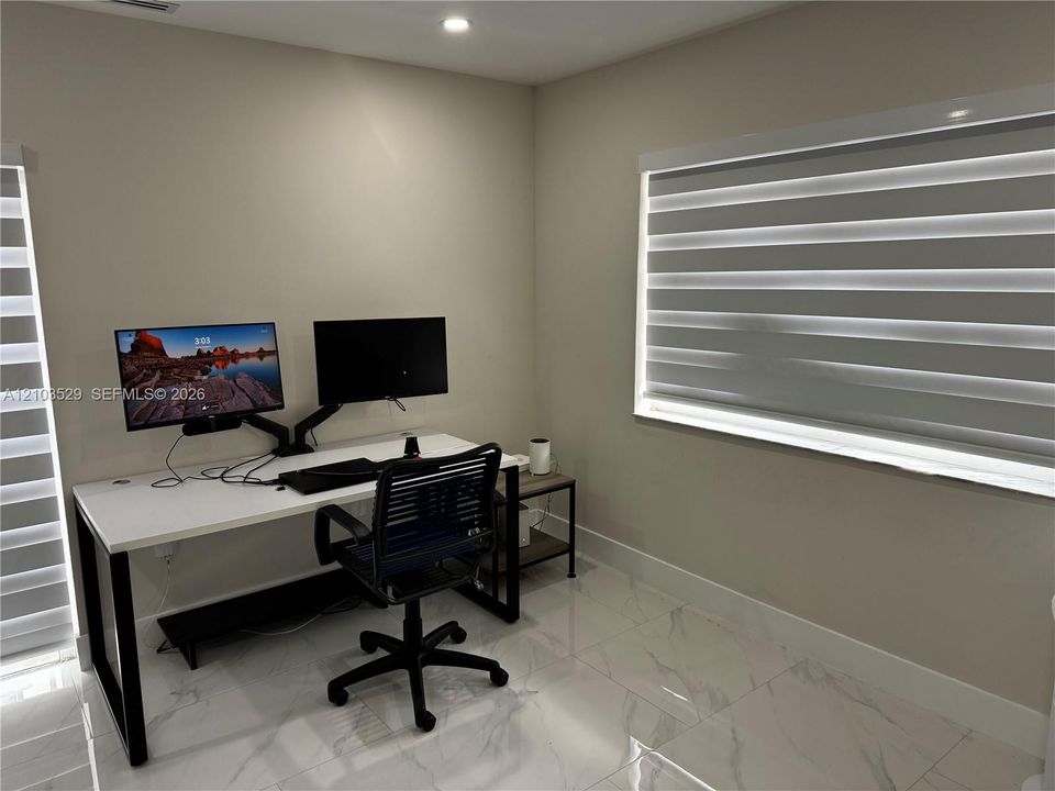 Neutral-toned interior space featuring light-colored stone-finish tile flooring, recessed ceiling lighting, and dual windows equipped with horizontal roller shades