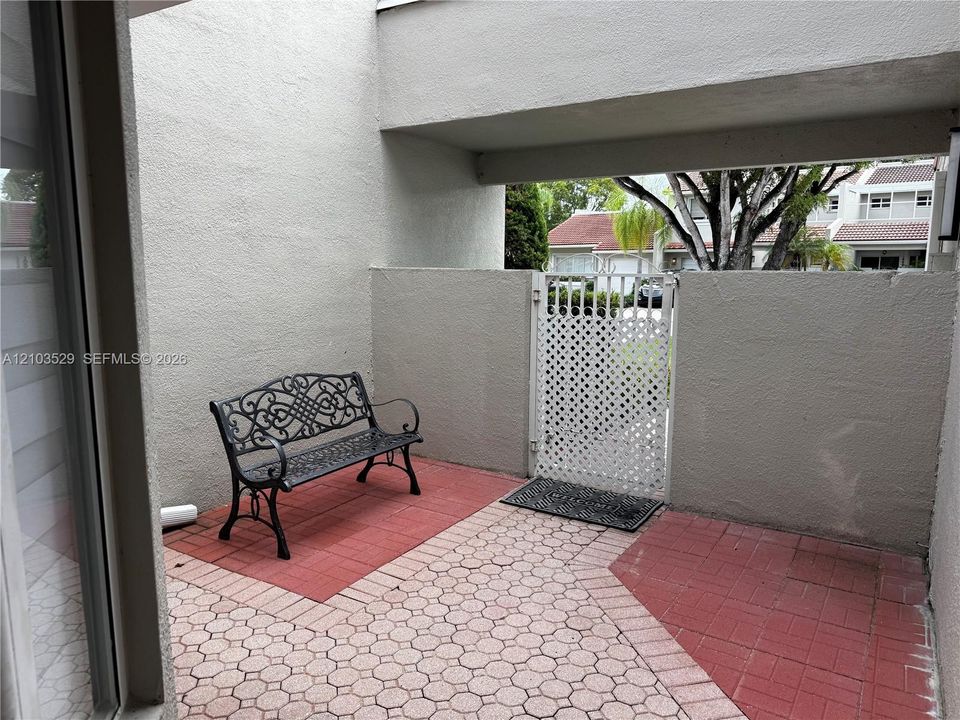 Private enclosed courtyard featuring decorative red brick and stone paver flooring, stucco privacy walls, and a white lattice metal gate
