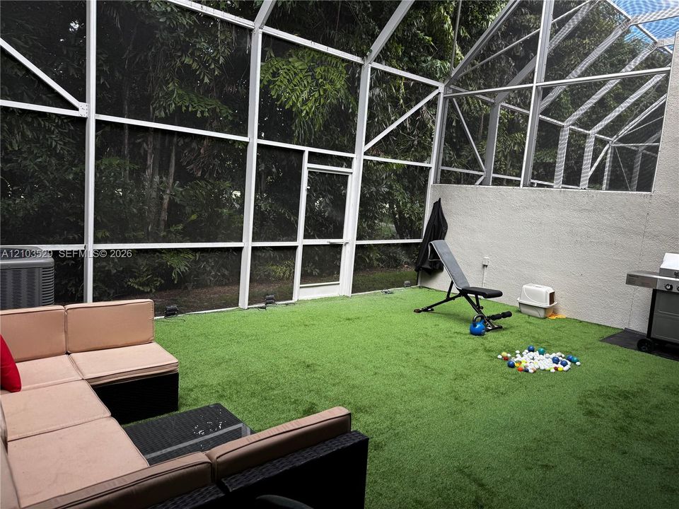 Screen-enclosed patio featuring synthetic turf flooring, textured stucco wall finishes, and a single-door access point