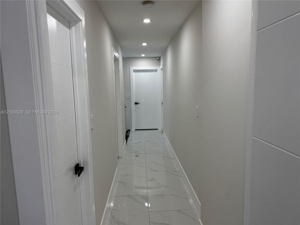 Hallway featuring large-format tile flooring with a neutral veined pattern, recessed ceiling lighting, and solid-core paneled doors equipped with matte black hardware