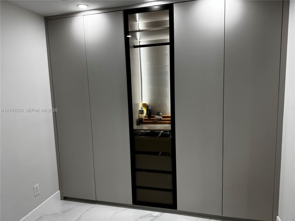 Floor-to-ceiling built-in cabinetry featuring matte-finish paneling, a central glass-front display section, integrated interior illumination, and internal pull-out storage drawers