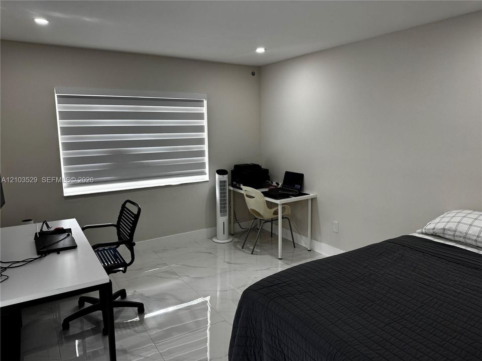 Neutral-toned interior featuring large-format polished tile flooring, recessed lighting, and a dual-shade roller window treatment