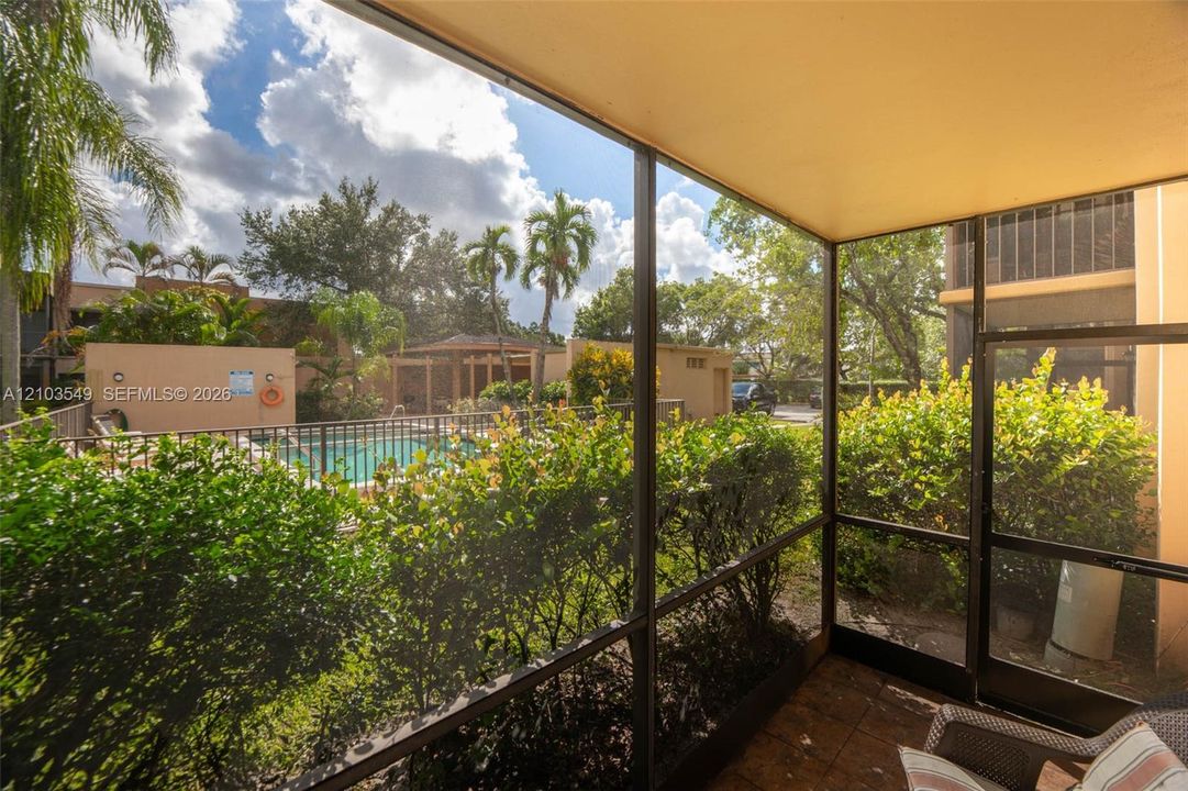 Screened-in patio featuring tile flooring, metal frame enclosure, and exterior access to a swimming pool and landscaped grounds
