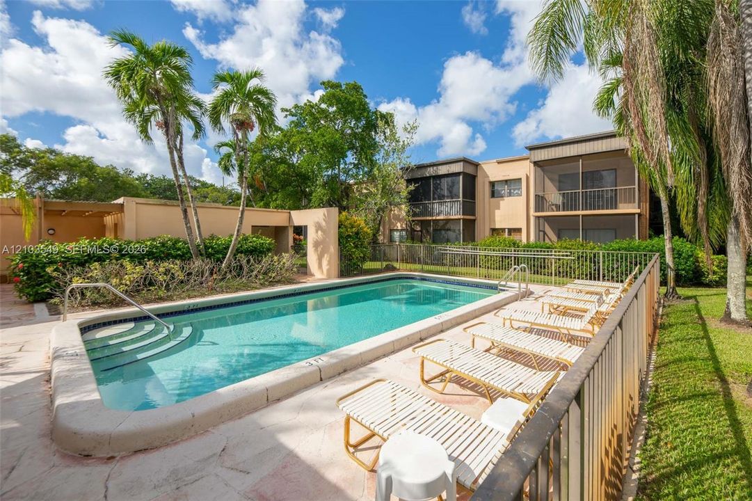 In-ground swimming pool with integrated stairs, surrounded by a stone-paver patio, perimeter fencing, and mature palm trees