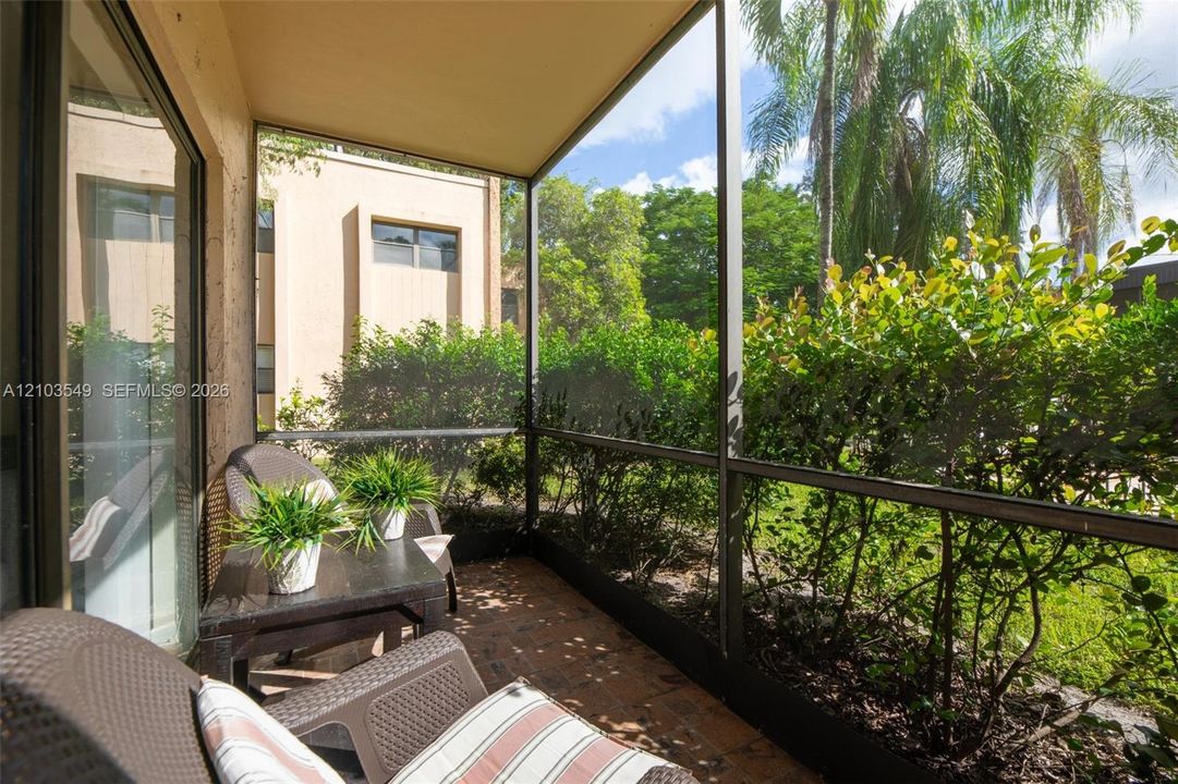 Screened-in lanai featuring brick pavers and exterior access to surrounding mature landscaping