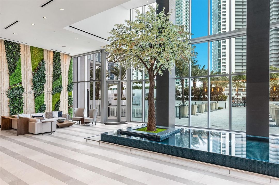 Spacious lobby featuring a vertical garden wall, large format tile flooring, a built-in water feature, and expansive glass curtain walls
