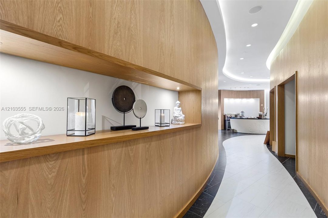 Wood-finish wall paneling with integrated display niche, recessed ceiling lighting, and a curved hallway design with contrasting floor tiling