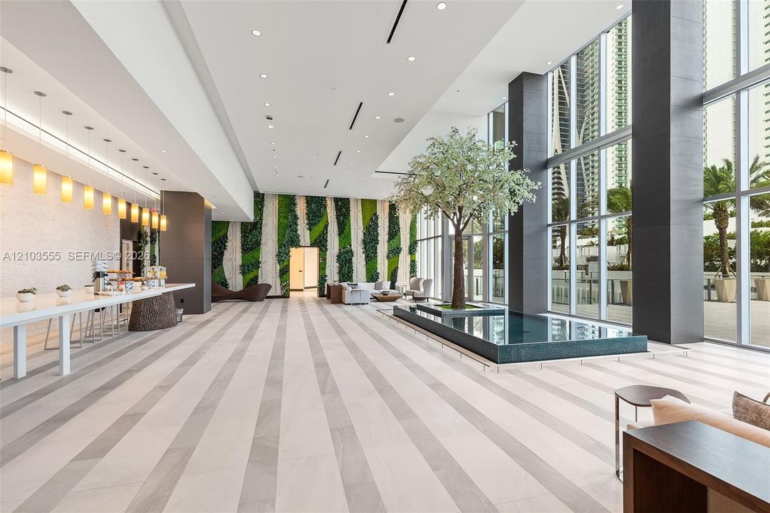 Expansive lobby featuring striped tile flooring, a living green wall, and a central water feature with an integrated tree