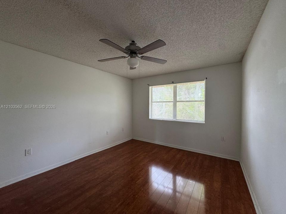 Room featuring wood-finish flooring, a ceiling fan with integrated light fixture, and a large window