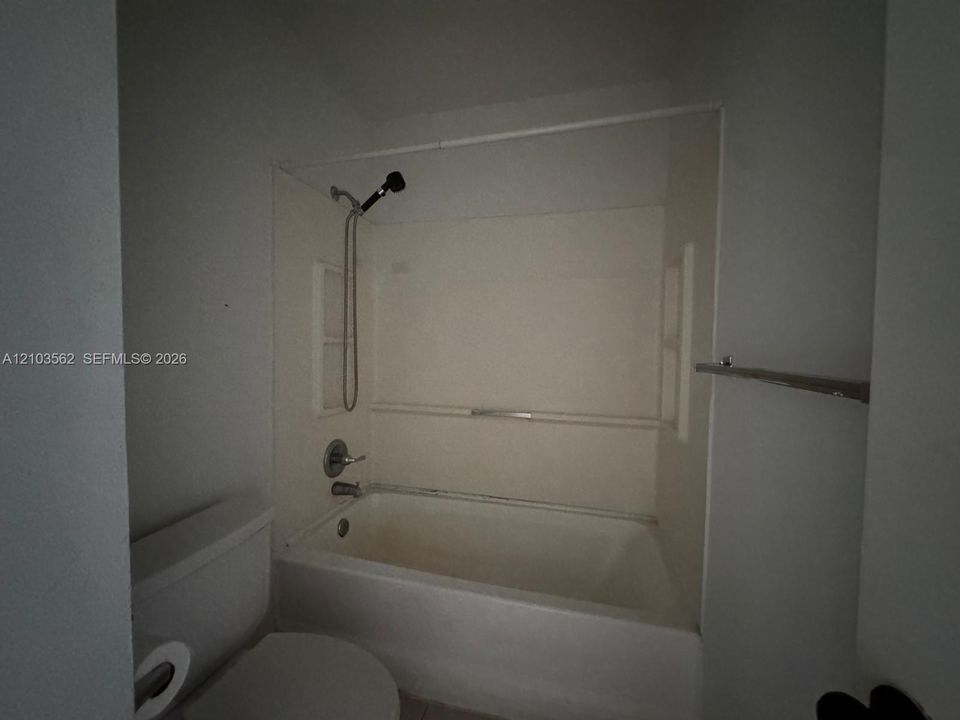 Full-size soaking tub with integrated surround, handheld shower fixture, metallic faucet hardware, and built-in wall-mounted towel rack