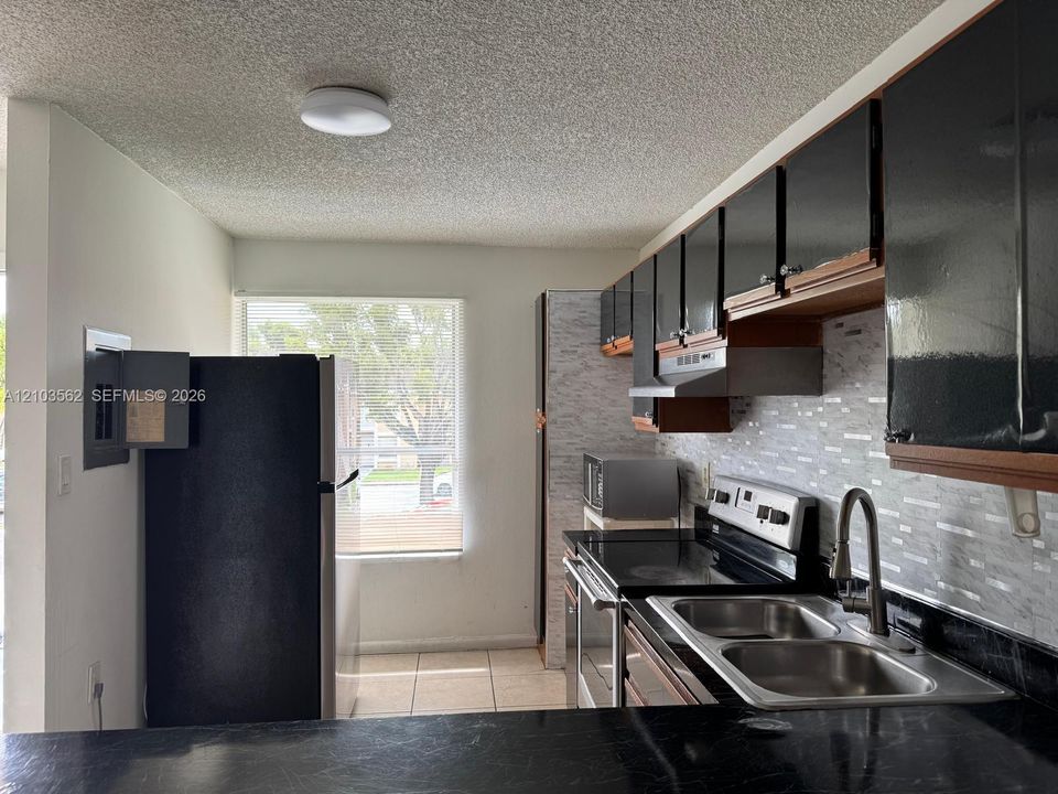 Kitchen featuring dark cabinetry, stone-finish countertops, stainless steel dual-basin sink with pull-down faucet, and a multi-toned linear tile backsplash
