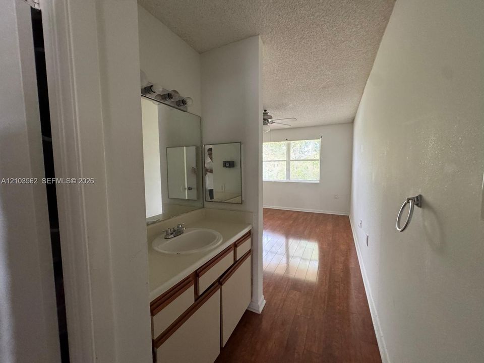 Vanity featuring a solid-surface countertop with an integrated basin, wood-trimmed cabinetry, wall-mounted mirror, and wood-finish flooring