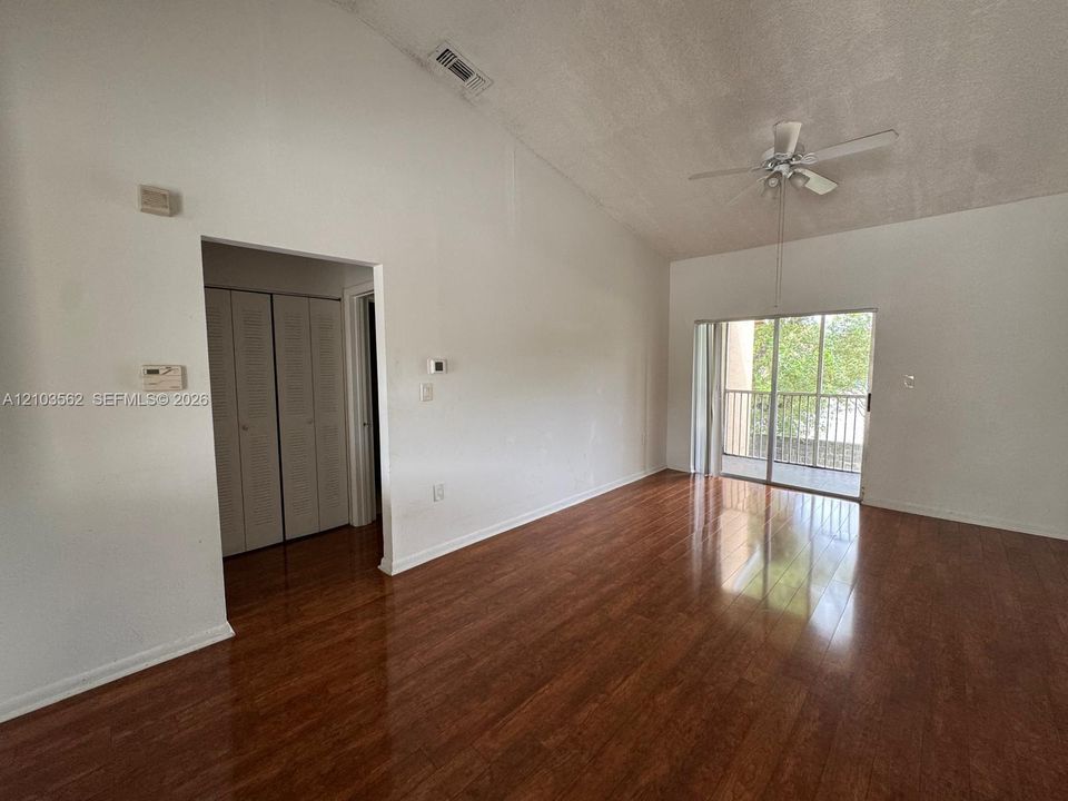 Vaulted ceilings, wood-finish flooring, sliding glass doors, and a ceiling fan