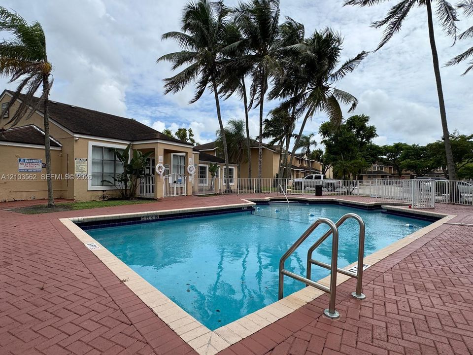 In-ground swimming pool featuring a brick-paver deck and stainless steel handrail