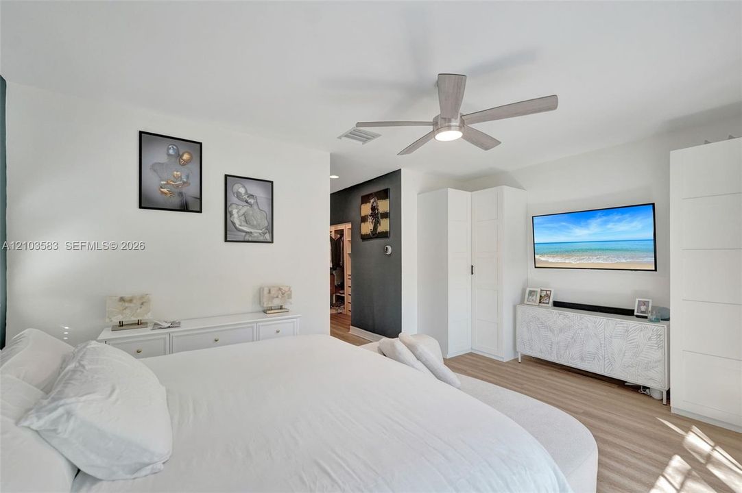 Room featuring wood-finish flooring, a neutral color palette, integrated ceiling fan with light, and built-in vertical storage cabinetry