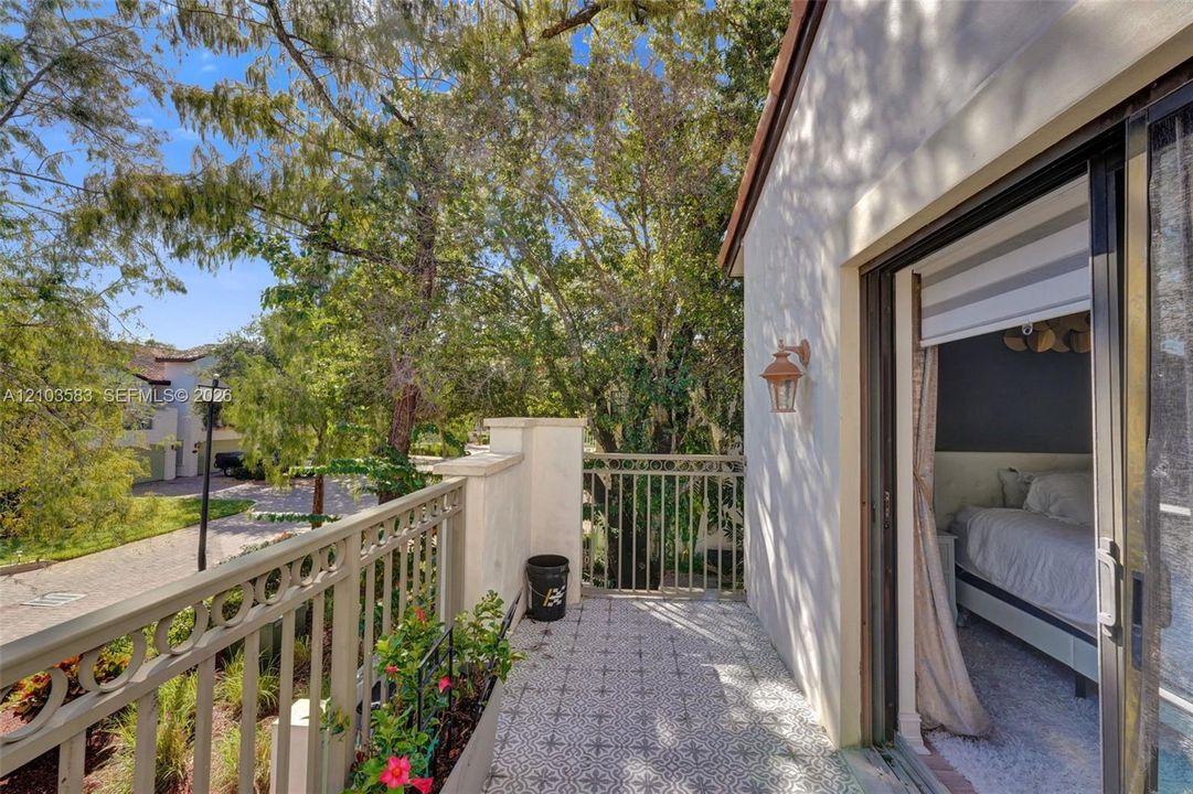 Private balcony featuring decorative tile flooring, ornate metal railing, exterior wall-mounted lighting, and sliding glass door entry