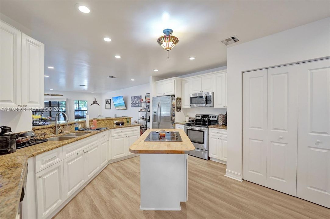Kitchen featuring white cabinetry, stone countertops, a center island with a cooktop, stainless steel appliances, and wood-finish flooring