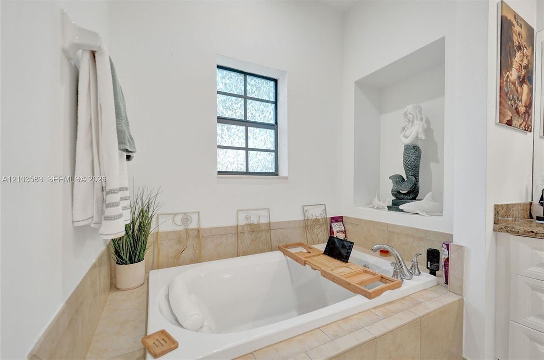 Drop-in soaking tub with a tiled surround, chrome faucet, and recessed wall niche