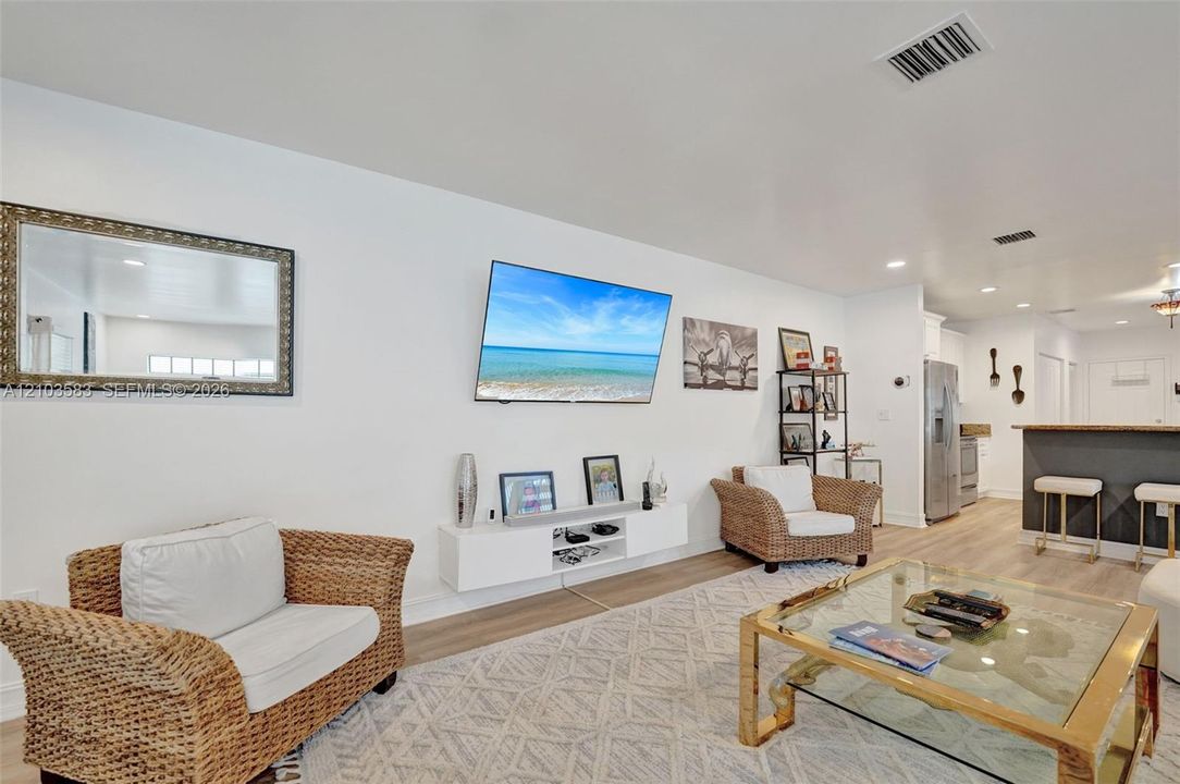 Open-concept interior featuring light-toned wood-finish flooring, recessed lighting, and a white floating media console