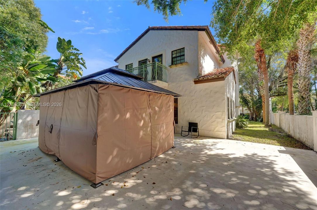 Stucco exterior featuring a second-story balcony with metal railing, a terracotta-tile roof, and a paved concrete patio area