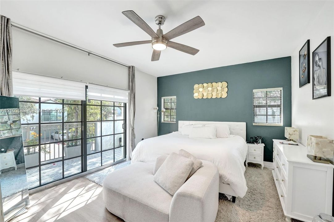 Large glass-paned sliding doors, ceiling fan with integrated lighting, wood-finish flooring, and dual wall-mounted windows