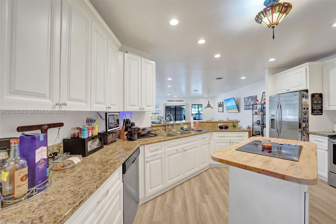 Kitchen featuring white shaker-style cabinetry, stone countertops, a central island with an integrated cooktop, stainless steel appliances, and wood-finish flooring