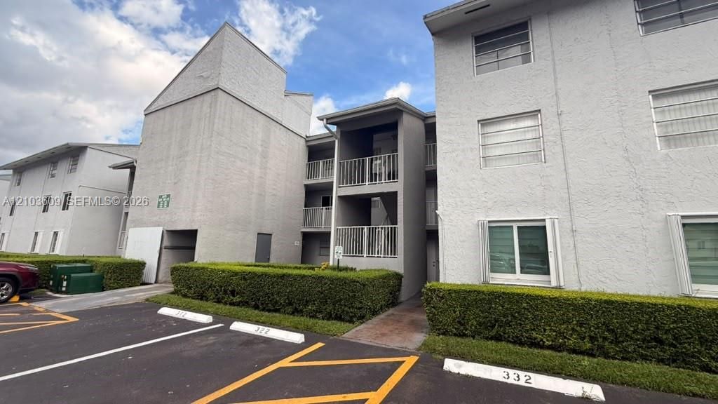 Multi-story stucco exterior featuring stacked private balconies, metal railings, and manicured hedge landscaping