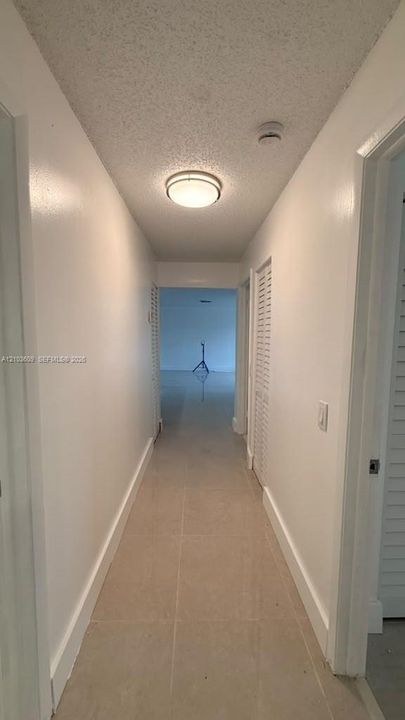 Hallway featuring neutral tile flooring, louvered bi-fold closet doors, and a flush-mount circular ceiling light