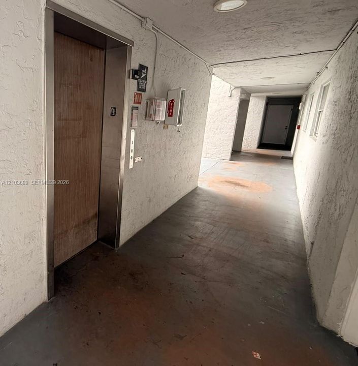 Covered walkway featuring an elevator with a wood-finished door, textured wall surfaces, and integrated recessed ceiling lighting