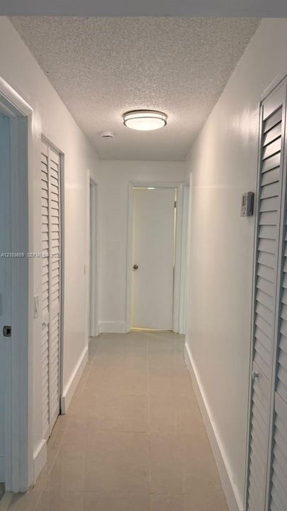 Hallway featuring neutral large-format tile flooring, textured ceiling, dual white louvered closet doors, and a flush-mount circular light fixture