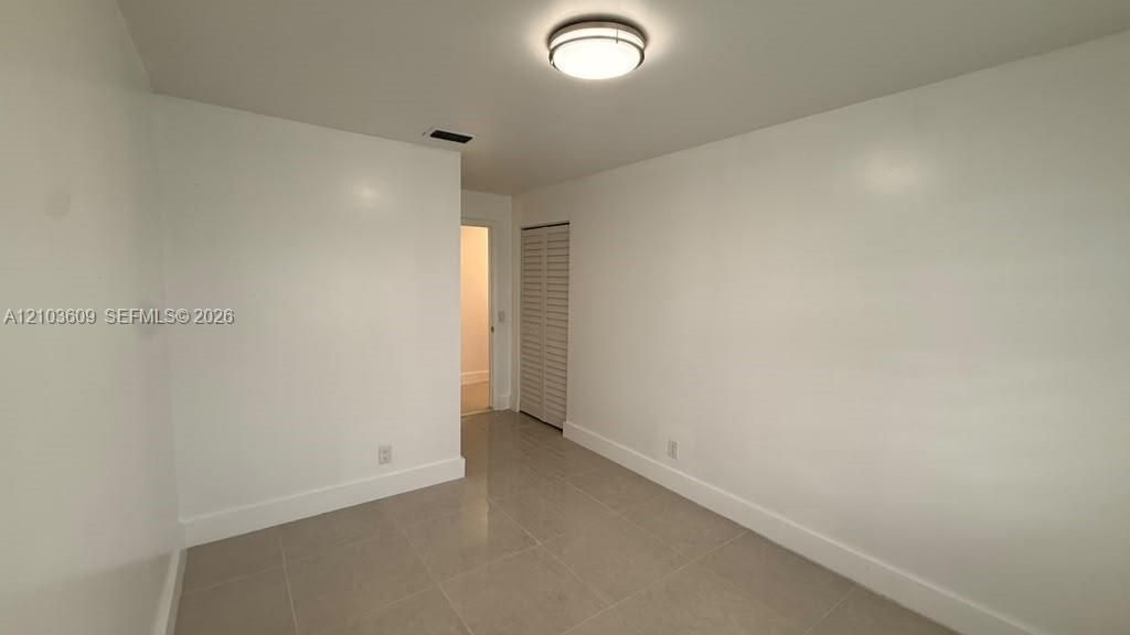 Neutral interior space featuring polished tile flooring, crisp white walls, a flush-mount circular ceiling light, and a bi-fold louvered closet door