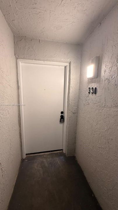 Exterior entryway featuring textured stucco walls, a solid-panel door, and a mounted square light fixture
