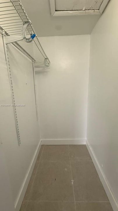 Storage space featuring ceramic tile flooring and white walls, equipped with wire shelving and an attic access panel