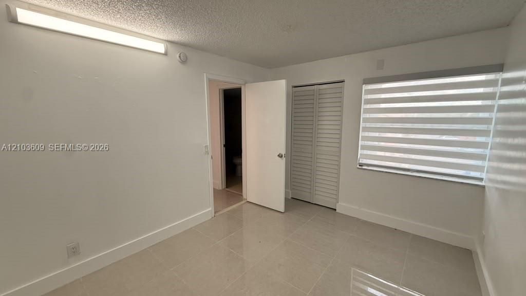 Interior room featuring large-format tile flooring, louvered bi-fold closet doors, wall-mounted linear lighting, and dual-layered window shades