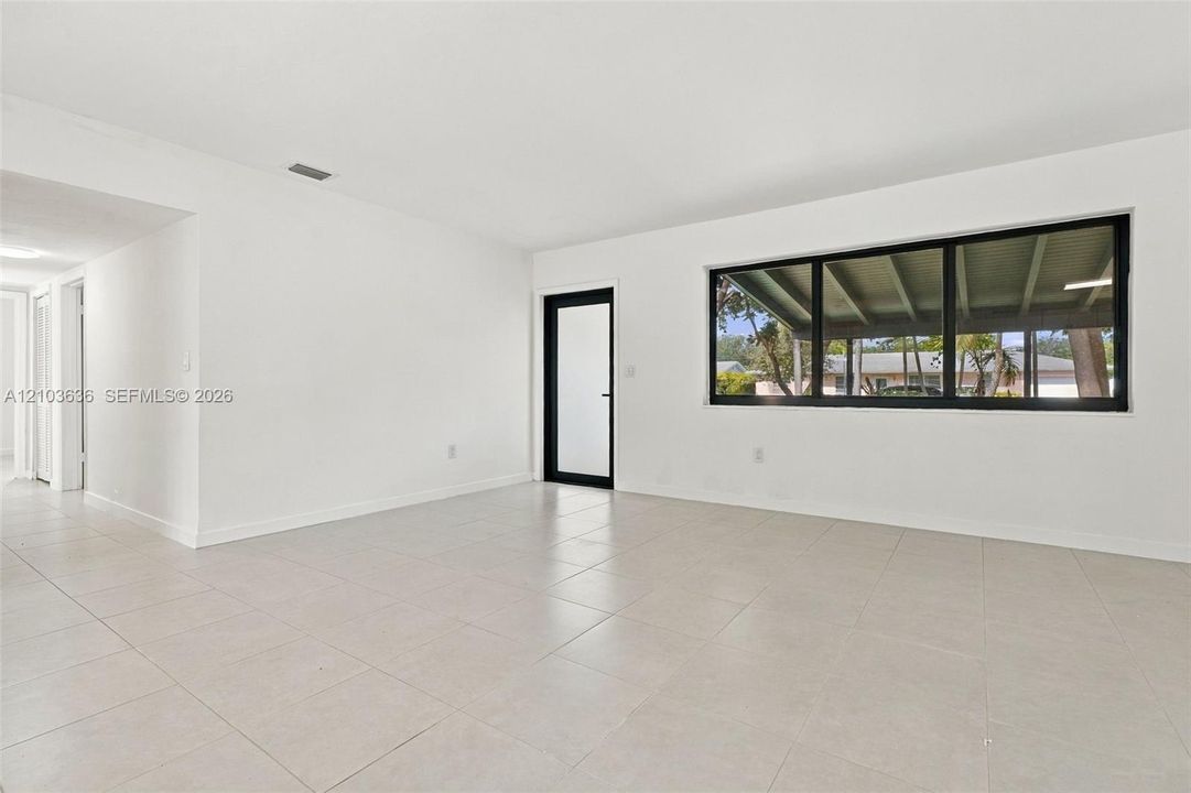 Interior space featuring large-format ceramic tile flooring, neutral walls, a prominent picture window with black framing, and a glass-paneled exterior door with a matching black frame
