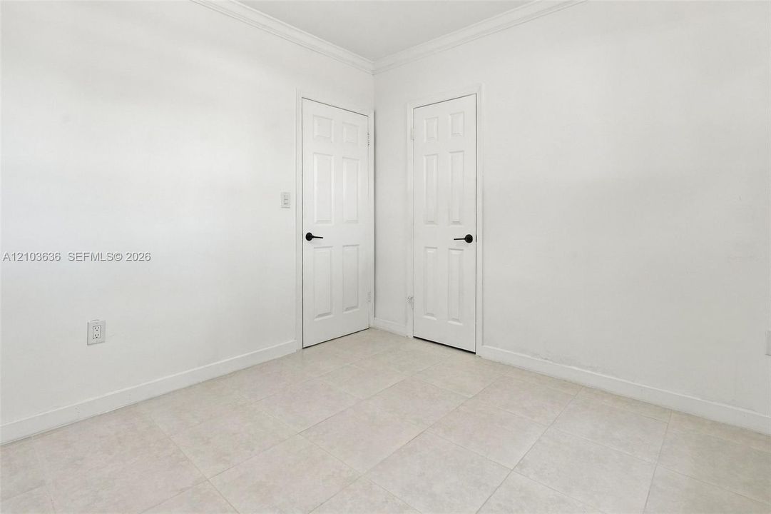 Neutral-toned tile flooring, two six-panel interior doors with matte black hardware, and crown molding