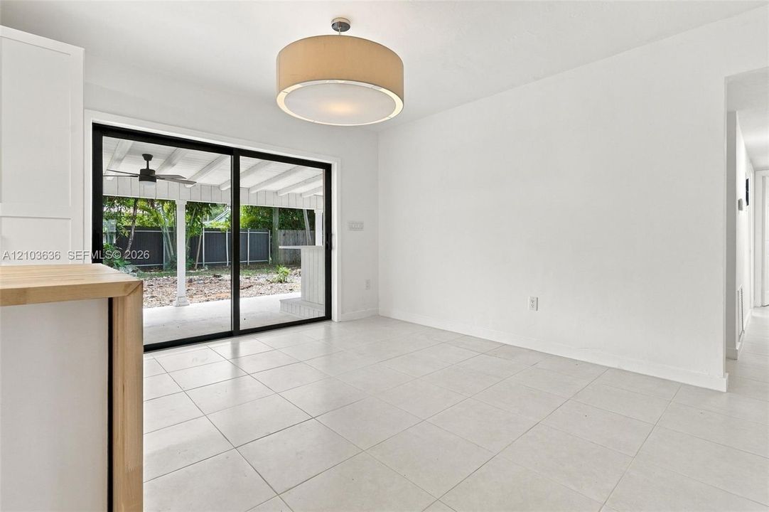 Neutral tile flooring, sliding glass door, drum-style pendant lighting, and kitchen cabinetry with a light wood-finish countertop