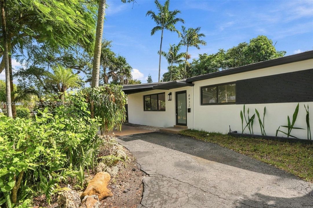 Exterior featuring a mid-century modern aesthetic, two-tone painted masonry, flat roofline, glass-panel entry door, and dark-framed windows