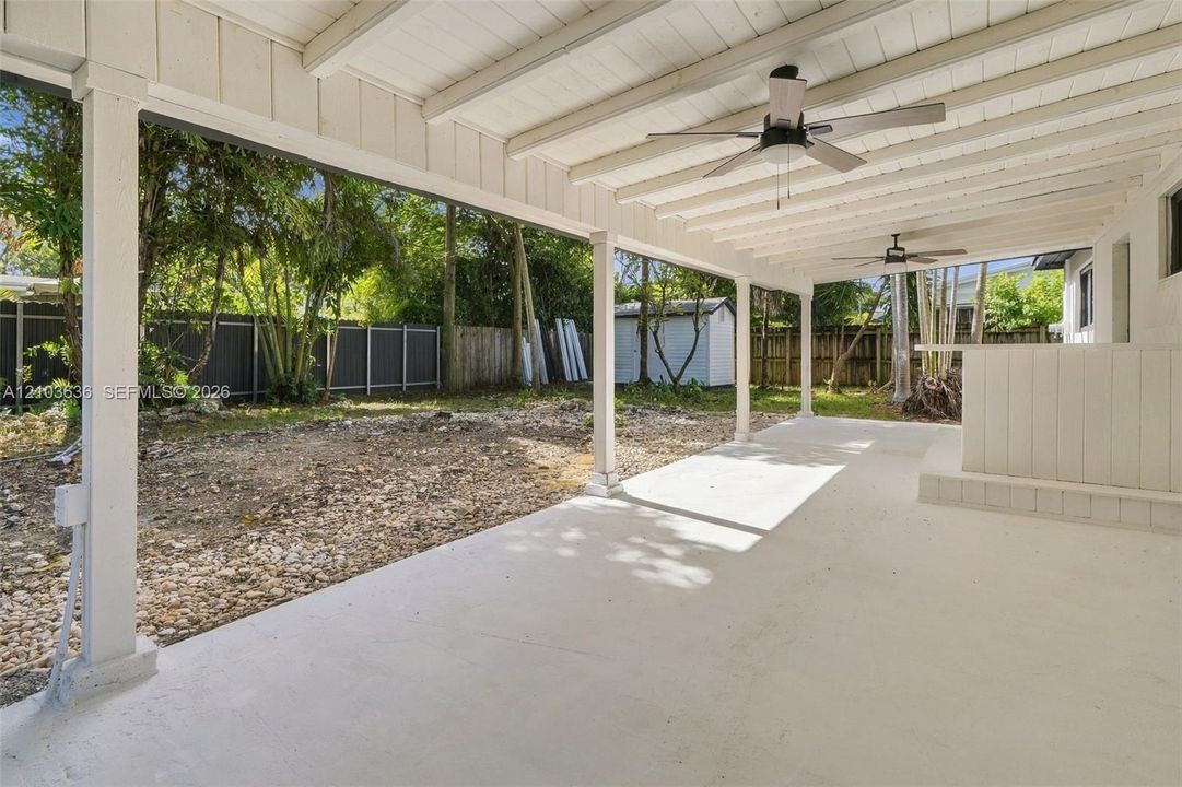 Covered concrete patio featuring a beamed ceiling, dual ceiling fans, and a built-in exterior bar