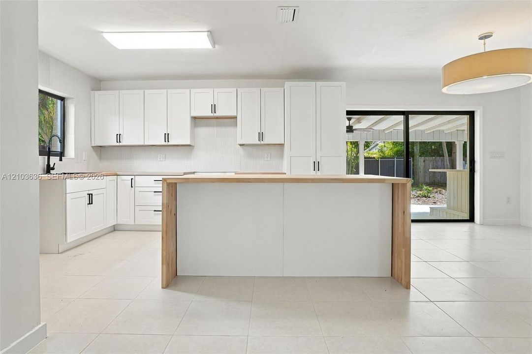 Kitchen featuring white Shaker-style cabinetry, a central island with a wood countertop, large-format tile flooring, a matte black kitchen faucet, and a sliding glass door