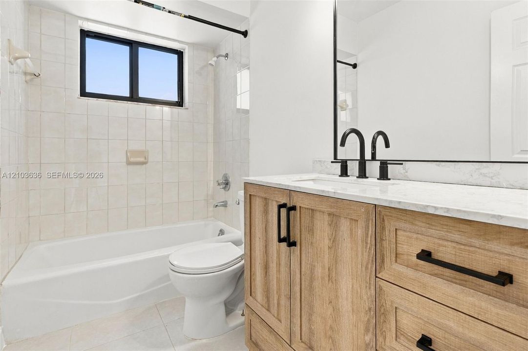 Bathroom featuring a wood-finish vanity with a stone-surface countertop, matte black hardware, square undermount sink, and tile-surround tub