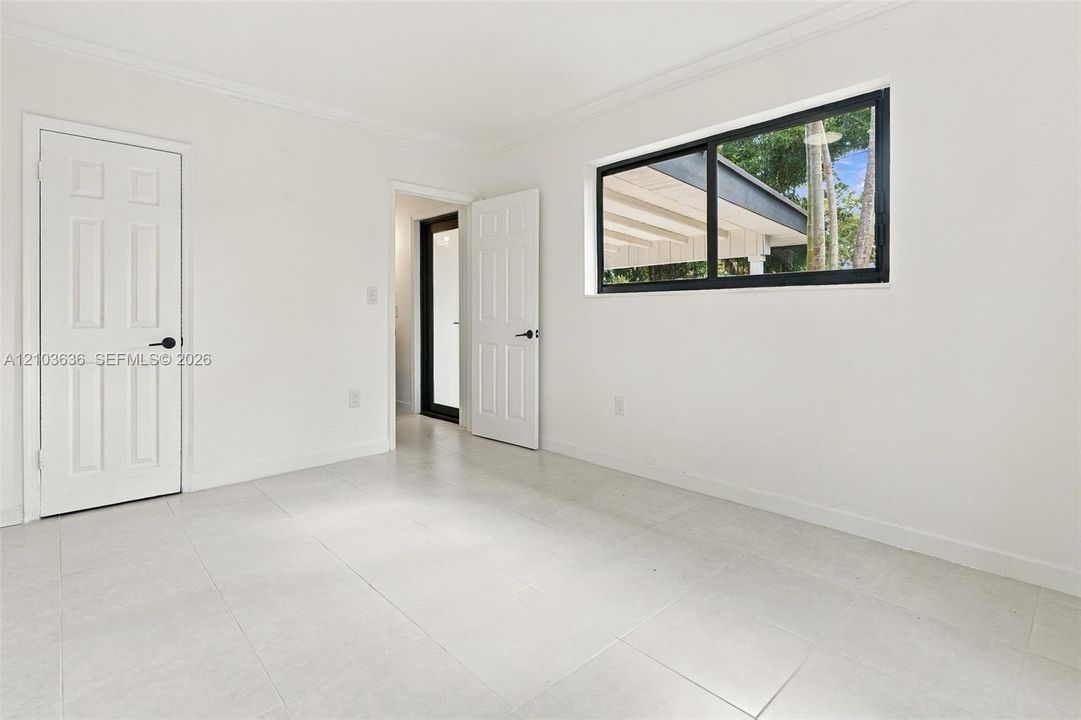 Interior space featuring neutral large-format tile flooring, white six-panel interior doors with matte black hardware, and a single-pane horizontal window with a black frame